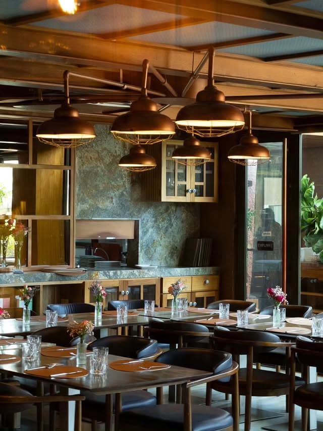 Salão do Le Cuisinier com luminárias de cobre, parede de pedra, mesas de madeira e flores