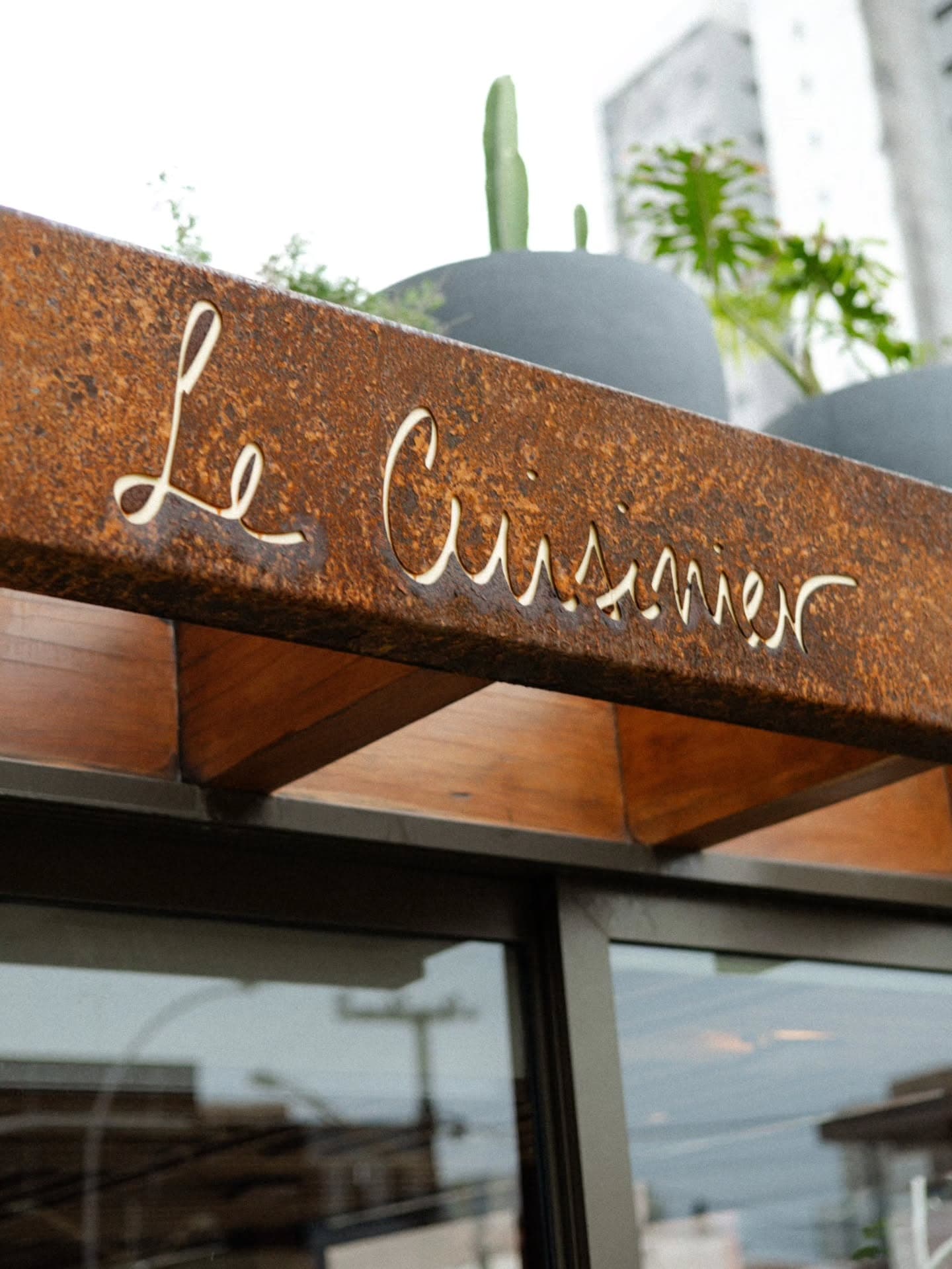 Letreiro vazado em aço corten com o nome Le Cuisinier na fachada do restaurante